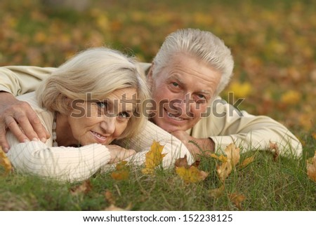 Happy mature couple resting on green grass in autumn park