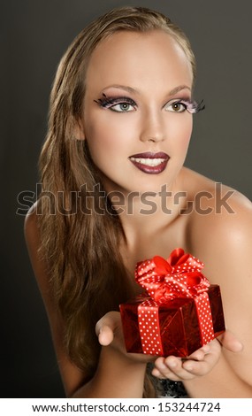 Young girl with a gift box and artistic makeup un dark background