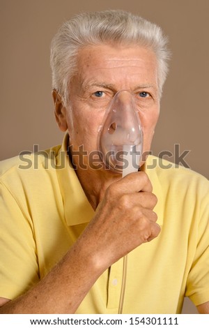 Elderly ill man making inhalation on beige background