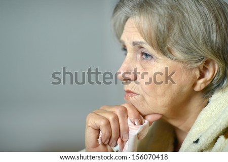 Close-up portrait of sad elderly woman on a gray background