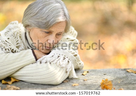 Sad elderly woman sitting at table in autumn forest