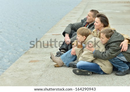Family of four sitting at river embankment in autumn