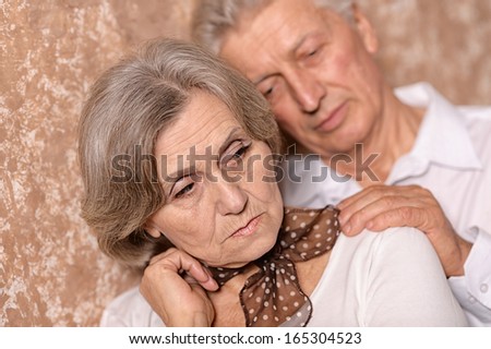 Close-up portrait of a sad elder couple on brown background