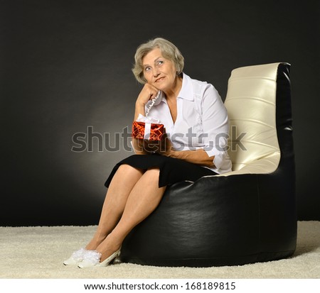 Happy elderly woman sitting with gift on black armchair