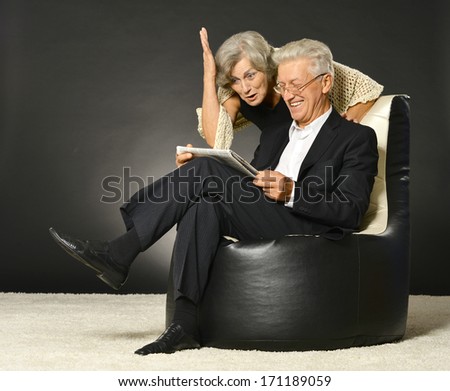 Senior couple reading newspaper sitting in black armchair on black background