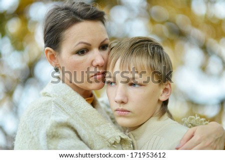 Beautiful sad mother with her son on a walk during the fall of the leaves in the park