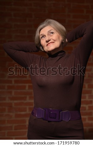 Happy smiling elder woman in elegant dress on brick background