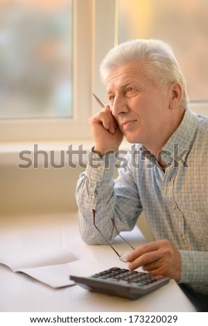 Serious elderly man with calculator sitting at table