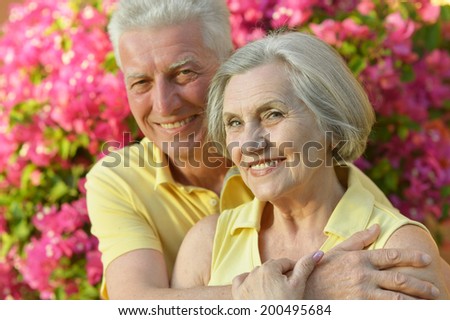 Happy elder couple resting on pink flowers background