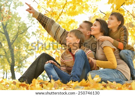 Family of four enjoying golden leaves in autumn park,man shows something