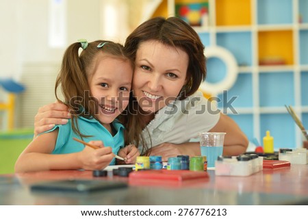 Portrait of a little girl painting with her mother