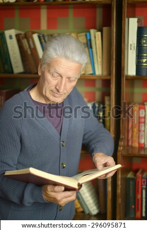 Portrait of elderly happy man with book over bookshelves