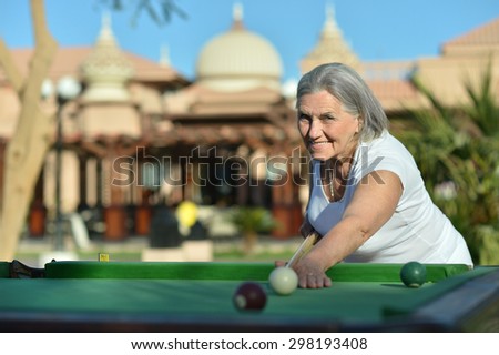Amusing senior woman on vacation playing billiards