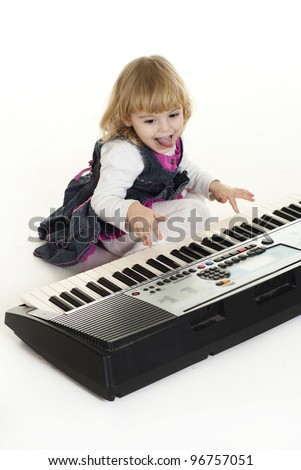 Cute little girl sitting on the floor near a synthesizer on a white background