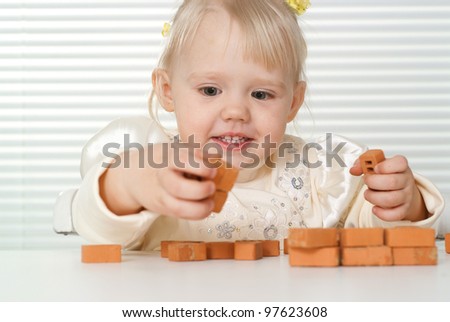 A small charming Caucasian baby sitting at the table and plays with the designer on a light background