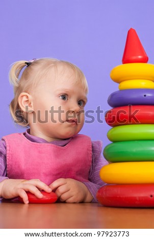 A little charming Caucasian baby sitting at the table and plays with a pyramid on a violet background