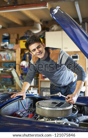 teenage boy leaning over the engine of a classic car in garage holding wrench