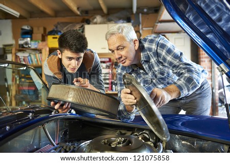 father and son working together on a classic car in a garage with air filter cover open looking in