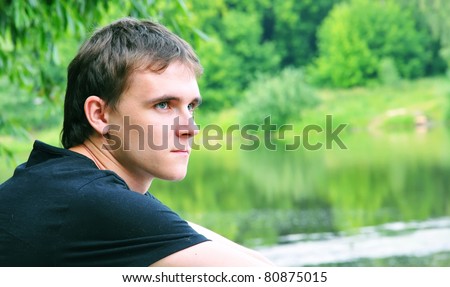 The beautiful young man with a thoughtful sight at the nature at lake