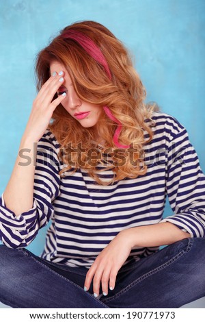 Beautiful girl with curly hair and a pink lock of hair dressed in a striped blouse posing on a blue background