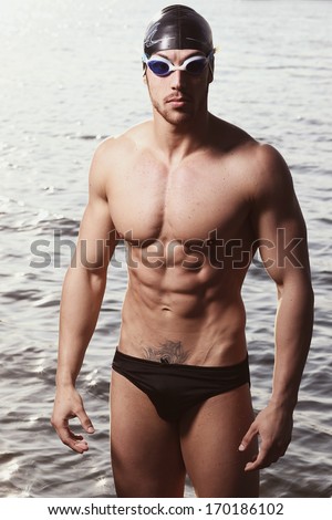 Stylized portrait of a young wet sexy muscular man standing in swimming pool