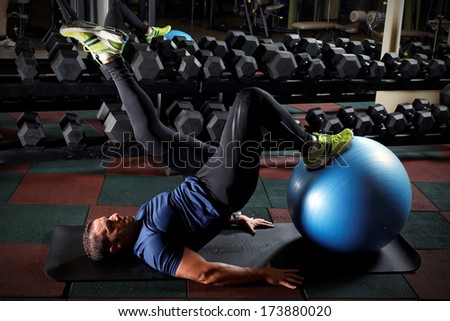 Man at the gym doing exercises for his abs with a Swiss ball.Low light.
