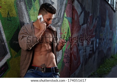 Sensual portrait of a very handsome muscular man with open shirt and hot body against window  on the phone in a ruins