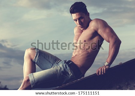 Handsome young muscle man shirtless with hand on rusty metal structure.Fashion colors.