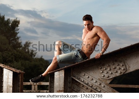 Handsome young muscle man shirtless with hand on rusty metal structure..Fashion photo