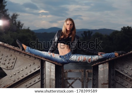 Slim gymnast girl in nature, sitting in the splits on the old bridge.Fashion photo.