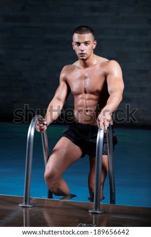 Stylized portrait of a young wet sexy muscular man standing in swimming pool .Shallow depth of field with focus on abdominals.