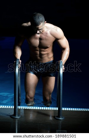 Stylized portrait of a young wet sexy muscular man standing in swimming pool .Shallow depth of field .