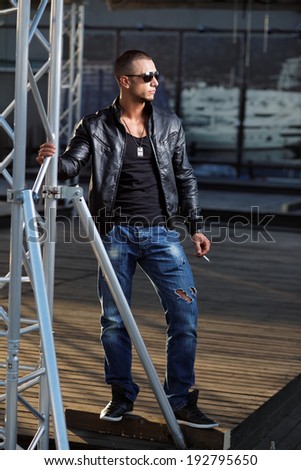 Attractive young muscle male model posing outdoors in black shirt and  leather jacket  .Fashion colors