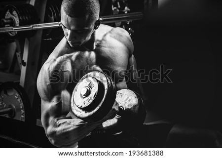 Closeup of a muscular young man lifting weights on dark background