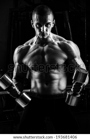 Closeup of a muscular young man lifting weights on dark background