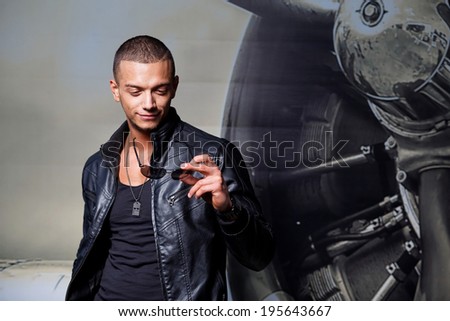 Attractive young muscle male model posing outdoors in black leather jacket and sunglasses .Fashion colors