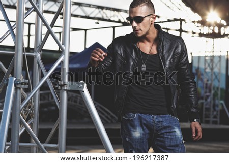 Attractive young muscle male model posing outdoors in black shirt and leather jacket.Fashion colors