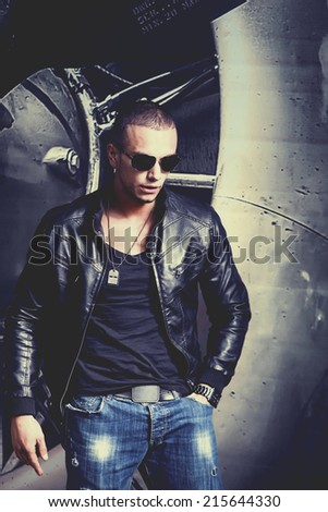Attractive young muscle male model posing outdoors in black shirt and leather jacket.Fashion colors