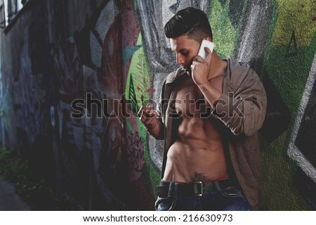 Sensual portrait of a very handsome muscular man with open shirt and hot body against window on the phone in a ruins