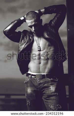 Attractive young muscle male model posing outdoors in  leather jacket.Fashion colors