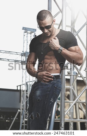Attractive young muscle male model posing outdoors in black shirt and sunglasses .Fashion colors