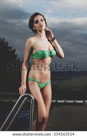 Beautiful long hair female model posing by the pool, outdoor portrait. Beautiful woman relaxing in a pool at summer