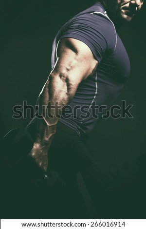 Handsome muscular bodybuilder.Muscular young man lifting weights on dark background. Fitness and workout concept.