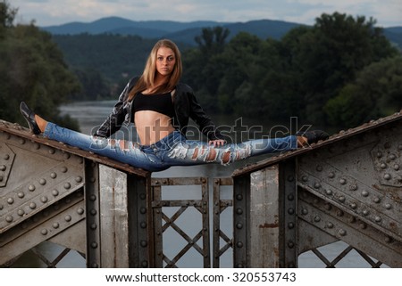 Slim gymnast girl in nature, sitting in the splits on the old bridge. Fashion photo.