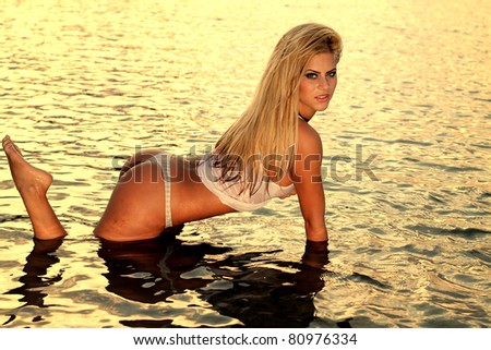 Beautiful blonde woman posing in the warm water of the lake at sunset