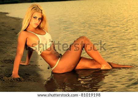 Beautiful blonde woman posing in the warm water at sunset