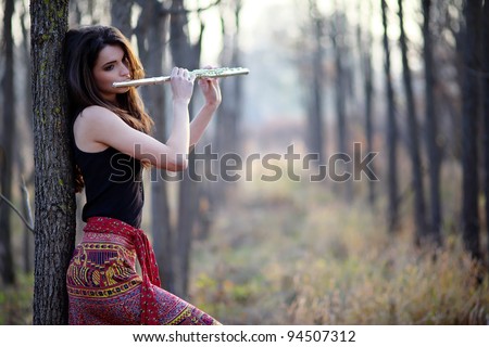 A beautiful woman in red skirt posing in a forest while playing on a flute.