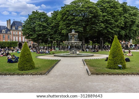 PARIS, FRANCE - JUNE 10, 2015: People relaxing on green lawns of famous Place des Vosges - oldest planned square in Paris, in Marais district. Place des Vosges was built by Henri IV from 1605 to 1612.