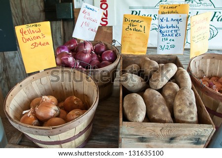 Roadside produce stand. Close up of baskets of onions and crate of potatoes with hand written signs identifying produce and price at a roadside produce stand in countryside adjacent to farm
