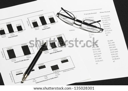business financial chart analysis with pen & eyeglasses on black table